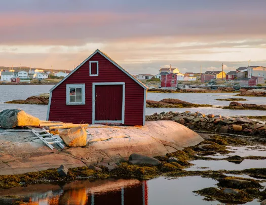 Rocky beach vista, numerous small houses in background, single red house wall in foreground.