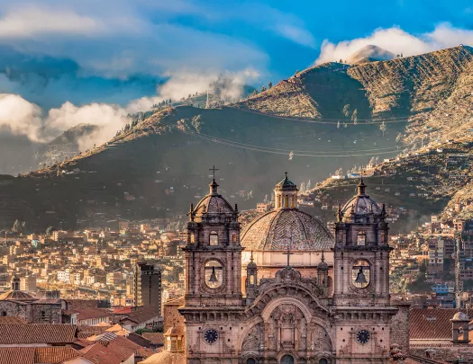 Wide shot of South American city, mountain range in distance, large cathedral in foreground. 