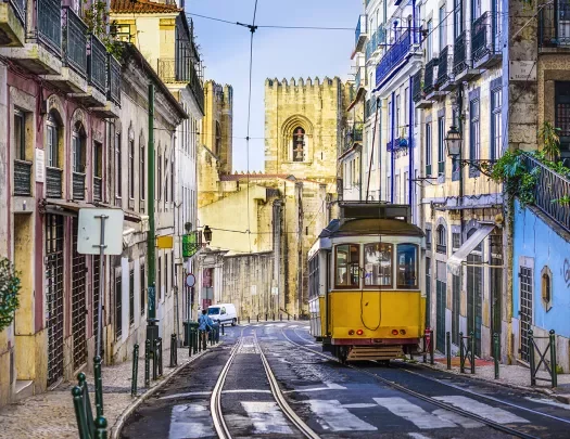 Street shot of Lisbon, Portugal. Tram, colorful buildings, stone tower in distance. 