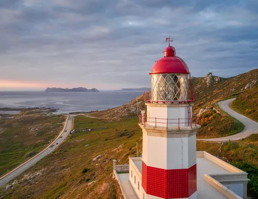 Wide shot of Spanish coastline during sunset, red and white lighthouse in foreground.