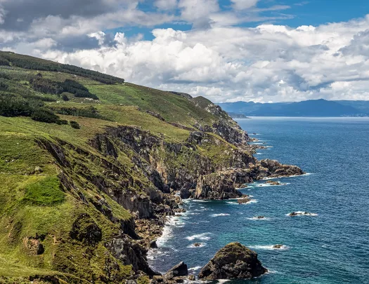 Shot of green, craggy coastline, ocean to right.