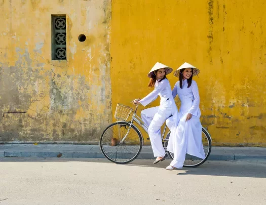Two women on a bike in front of a yellow wall in Vietnam