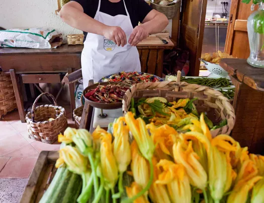 Local chef preparing food, zucchini + blossoms in foreground. 