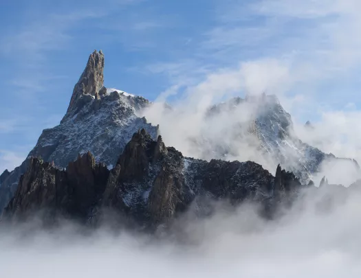 Wide shot of large, craggy mountain range, clouds covering.