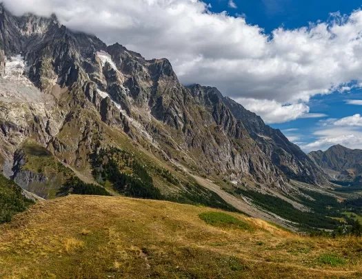 Wide shot of craggy mountains, golden hills in foreground. 