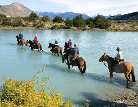 Group of guests on horseback, trekking through cloudy lake.