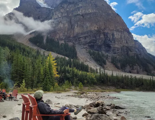 Guest sitting on sandy lakeshore, large mountain in distance.