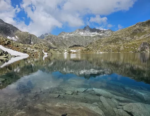 Shot of still lake, craggy rocks dotting lakeside, mountain in distance.