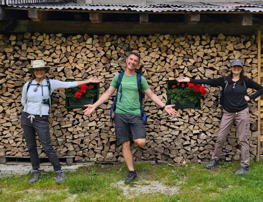 Three guests in front of wooden building, one in center, the other two gesturing to them.