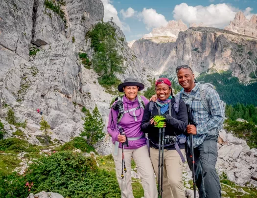 Three guests in hiking gear, craggy cliffside to their right.