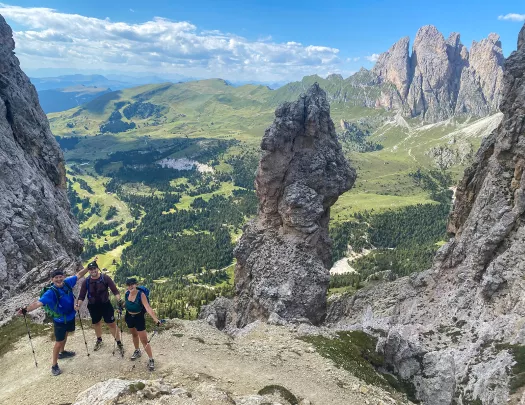 Three guests on mountaintop overlooking large valley, craggy peaks around them.