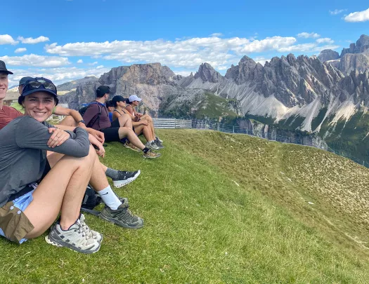 Guests sitting on hillside, overlooking meadow, sharp, craggy peaks behind them.