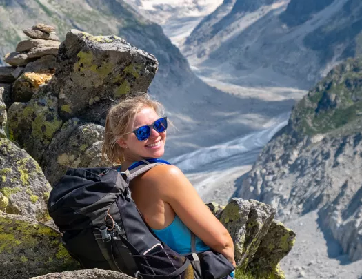 Young guest sitting on rock, smiling at camera, large mountain valley in distance. 