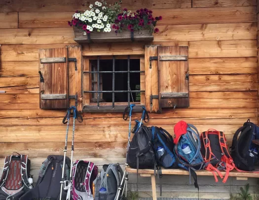 Hiking backpacks piled in front of log cabin.