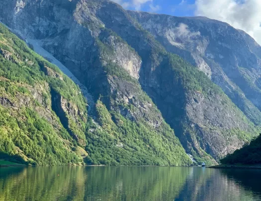Blue sky and mountainside reflected in a clear Norwegian fjord