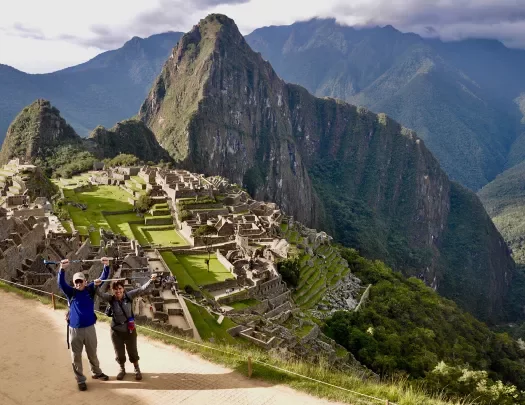 Two guests holding hiking poles over their heads in celebration, Machu Picchu in background.