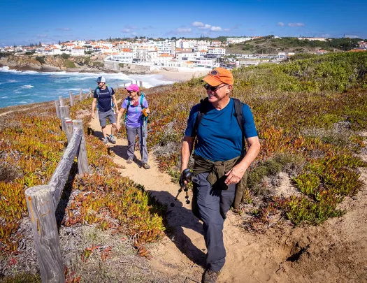 Three guests walking along ocean cliff, beach town behind them.