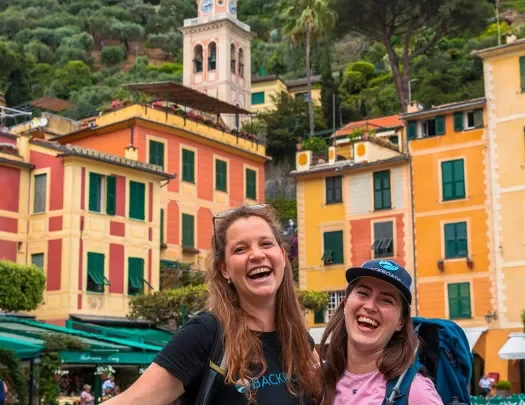 Two smiling guests in front of colorful buildings.