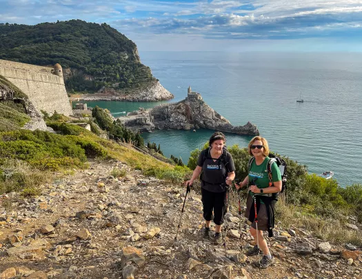 Two guests on rocky cliffside, Chiesa di San Pietro in distance.