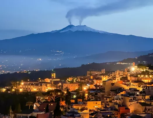Nighttime shot of Italian hillside town, smoking volcanoes in distance.
