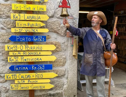 Local in hiking gear ringing bell, assortment of direction signs to his right.