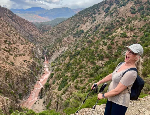 Guest at valley cliffside, gesturing towards river running through.