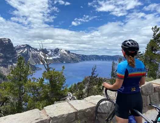 Woman standing with her bike looking out towards a lake and mountains