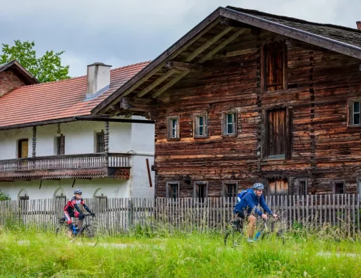 Two people riding their bikes in front of wooden and stone houses