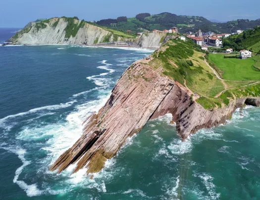 Slanted cliff on the coast of an ocean, with a small town in the distance