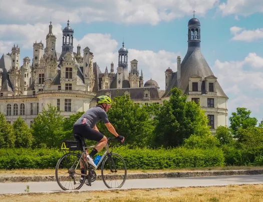 Man biking on an asphalt road, with a rustic, castle-like building in the background