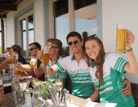 Man and women wearing a bicycle jersey, holding up glasses full of beer