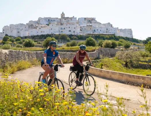 Two women riding bikes with an ancient building in the background