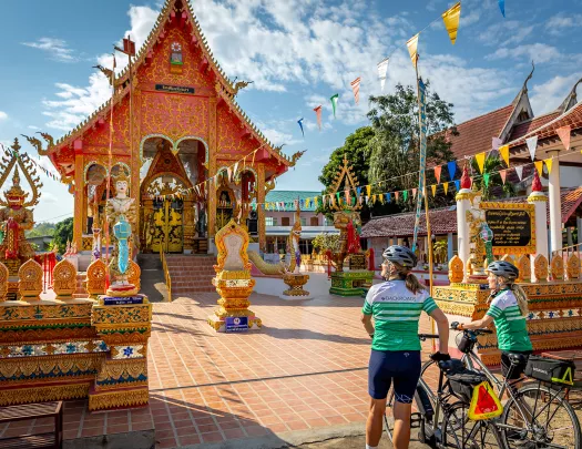 Two women walking their bikes as they approach a shrine