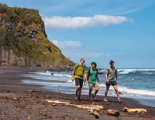 Three men walking on a beach, with a large cliff in the background