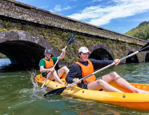 Two men on a kayak, paddling in a river by a bridge