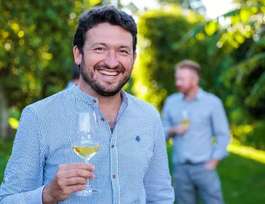 Man smiling at the camera while holding up a glass of wine