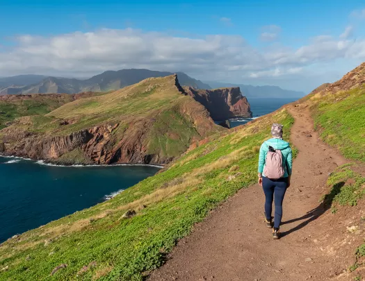 Woman walking on a dirt path on a hill, with a lake on the ground level