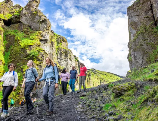 Group of 6 people descending down a dirt and rock trail, with large cliffs on either side of them