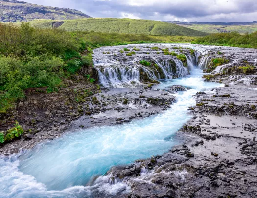 Small waterfall with an active river in the middle of a grass field