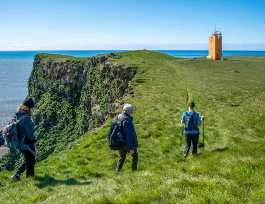 Three people walking on a grassy field on top of a cliff, with an orange building in the distance