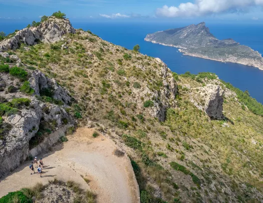 Group of people hiking on a trail along a cliff, with the ocean and an island in the distance