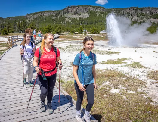 One woman and two girls hiking next to an active geyser