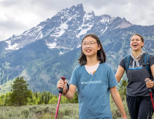 Woman and girl with walking poles hiking in a grassy valley