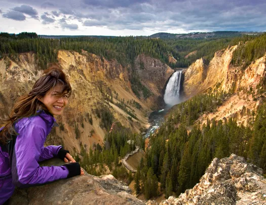 Woman smiling while leaning over a rock on top of a cliff