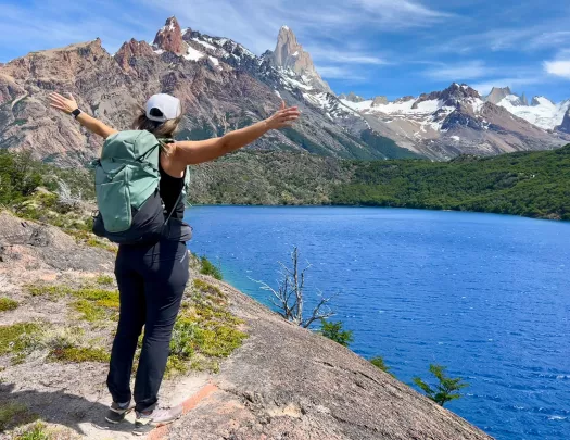 A person holds their arms wide open to a blue lake