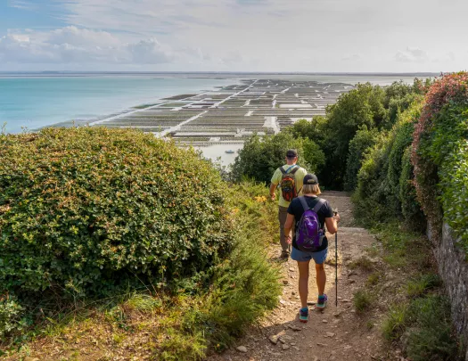 Man and woman descending down a dirt trail towards the ocean