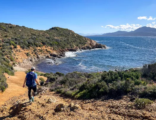 Man descending a dirt path towards a beach surrounded by trees