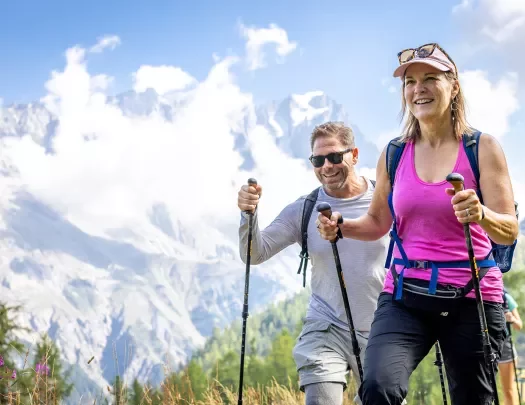Man and woman with walking poles ascending a grassy mountain