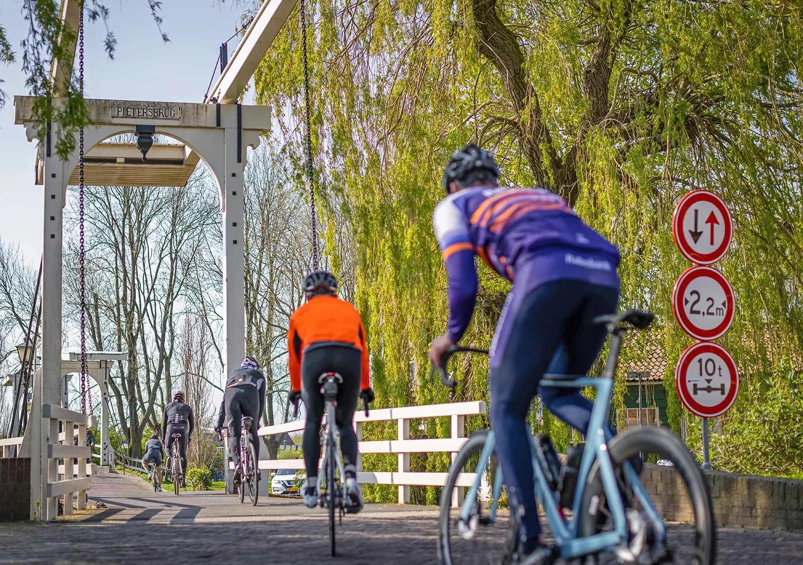 Five cyclists biking across a wooden bridge.