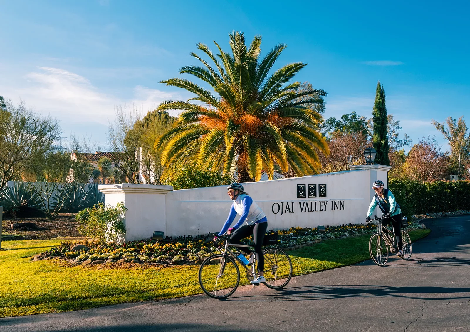 Two guests cycling past Ojai Valley Inn sign.
